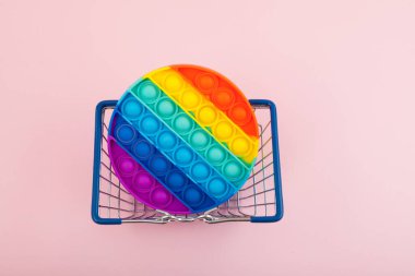 Silikon renkli anti-stres oyuncağını alışveriş sepetine koy. Pop Bubble 'ı it. Pembe arkaplan, metin için boşluk. Basit gamze.