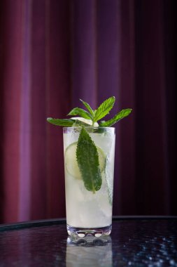 Camda Mojito kokteyli bulunan uzun camlar cam masanın kenarında duruyor. Tazeleyici yaz içeceği. Seçici odaklanma, dikey yönelim. 