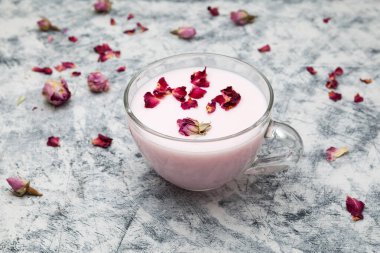 Açık fincanda pembe ay sütü, gece yarısı rahatlatıcı içecek, güller, gri desenli arka plan, seçici odak.