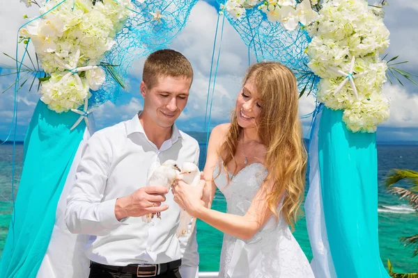 The happy bride and groom with white doves on a tropical beach u — Stock Photo, Image