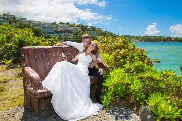 Noiva feliz e noivo sentado no banco na frente da bela — Fotografia de Stock