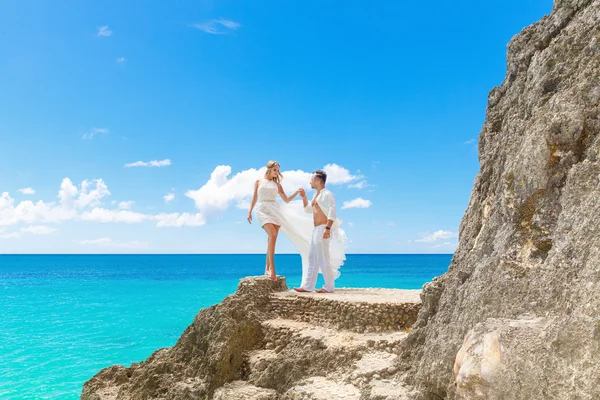 Glücklicher Bräutigam und Braut auf dem Felsen. türkisfarbenes Meer im Hintergrund — Stockfoto