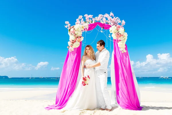 De ceremonie van het huwelijk op een tropisch strand in paars. Gelukkige bruidegom en — Stockfoto