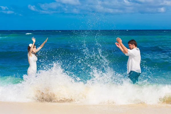 Lyckliga bruden och brudgummen ha kul i vågorna på en tropisk strand — Stockfoto