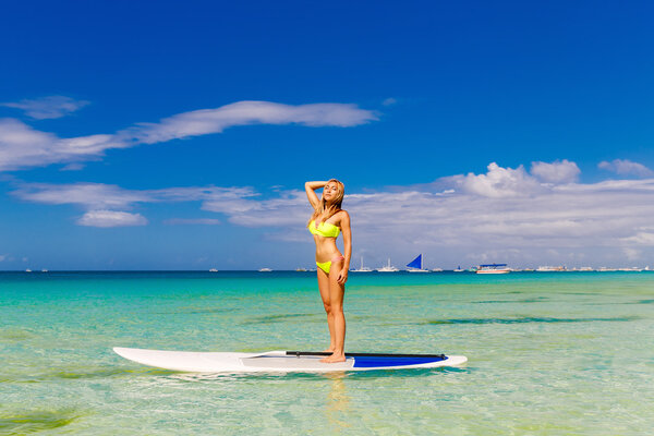 Happy beautiful young girl with paddle board on a tropical beach