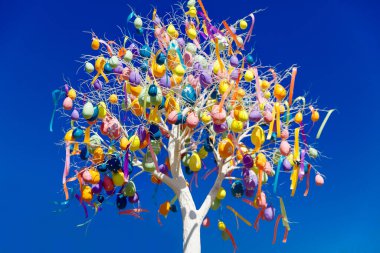 Renkli Paskalya yumurtaları mavi bahar gökyüzüne karşı bir ağaçta asılı duruyor. Bahar tatilleri için şehrin sokak dekorasyonunun kutlaması. Mutlu Paskalyalar.