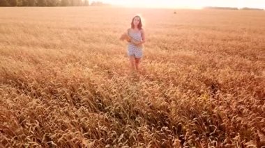 Genç ve güzel bir kız gün batımında altın olgun buğday tarlasında yürüyor..