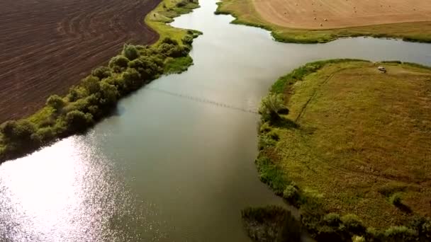 Vista aérea desde el dron de un campo achaflanado y pajar después de cosechar cultivos de granos, un río y un campo arado al atardecer. El concepto de cosecha de granos en la industria agrícola y — Vídeos de Stock