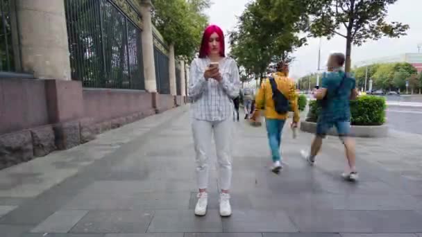 Tijdsverloop van eenzaamheid rood haar tienermeisje staan in het centrum van de stad in drukke straat met behulp van smartphone, terwijl menigten van mensen lopen door. — Stockvideo