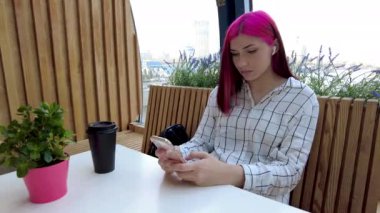 Üzgün, kızıl saçlı, akıllı telefonlu bir kız sosyal ağlarda, kafede oturmaktan sıkılıyor..