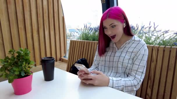 Tråkig rödhårig student flicka med smartphone sitter på café glad att få goda nyheter på sociala nätverk. — Stockvideo