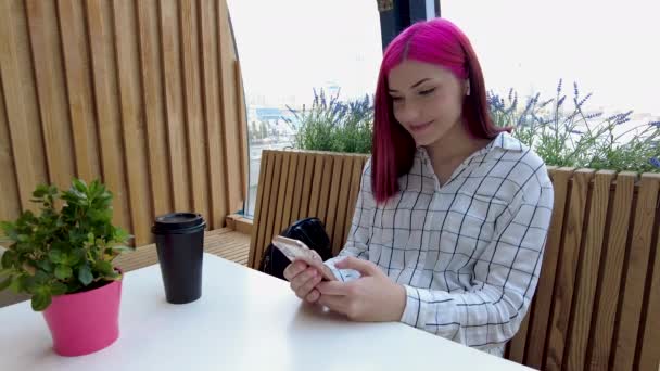 Glad rödhårig student flicka chatta på en smartphone i sociala nätverk sitter på café. — Stockvideo