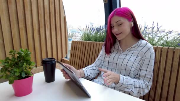 Schöne rothaarige Studentin kommuniziert mit Freunden per Videochat auf dem Tablet in sozialen Netzwerken, die im Café sitzen. — Stockvideo