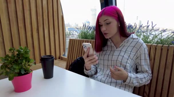 在社交网络上，红头发的女学生坐在咖啡店里，与男朋友在智能手机上咒骂. — 图库视频影像