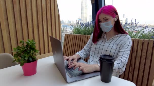 漂亮的红头发女学生戴着面罩，在咖啡店里担任远程员工，带着笔记本电脑。病毒感染大流行性流感病毒2019-ncov. — 图库视频影像