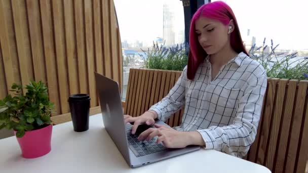 Belle étudiante rousse travaille comme employée à distance avec un ordinateur portable et un casque sans fil dans un café. — Video