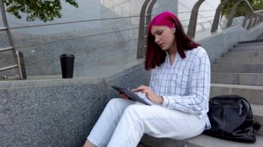 Şehirdeki basamaklarda tabletle oturan üzgün kızıl saçlı kız sosyal ağlarda iyi haberler almaktan mutlu..