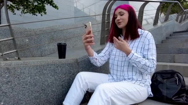 Vackra rödhåriga influencer bloggare flicka talar gör videosamtal med hjälp av smartphone med sina abonnenter i sociala nätverk sitter på trappan i staden. — Stockvideo