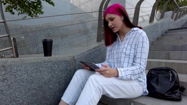 Die schöne rothaarige Studentin arbeitet als Angestellte mit Tablet auf den Treppen der Stadt. Videokonferenz mit Kollegen. — Stockvideo