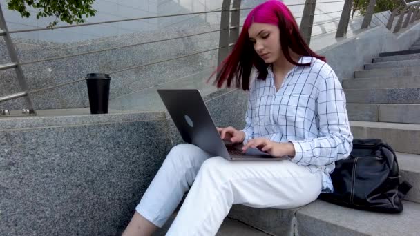 在城市的台阶上，漂亮的红头发女学生像个远程员工一样坐在笔记本电脑上工作. — 图库视频影像