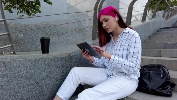 Smutna, samotna, rudowłosa studentka z tabletem nudzi się w serwisach społecznościowych siedzących na schodach w mieście. — Wideo stockowe