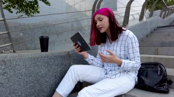 Vervelende roodharige student meisje zweert met haar vriend op een tablet in sociale netwerken zitten op de trappen in de stad. — Stockvideo