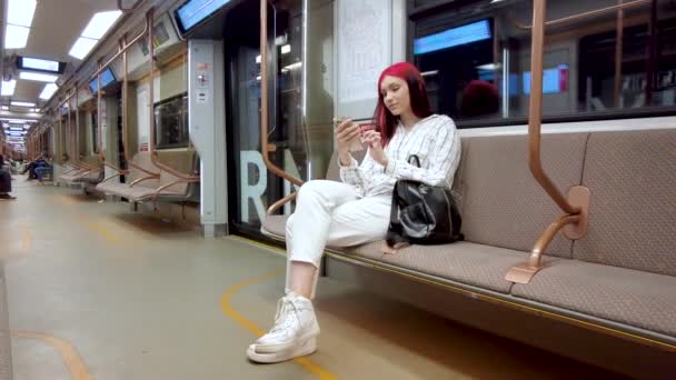 Moskva, Ryssland 25 augusti 2021 Vacker rödhårig student flicka i tunnelbanan i covid19 ansiktsmask och chatta på smartphone i sociala nätverk.Virusinfektion pandemisk influensa coronavirus 2019-ncov. — Stockvideo