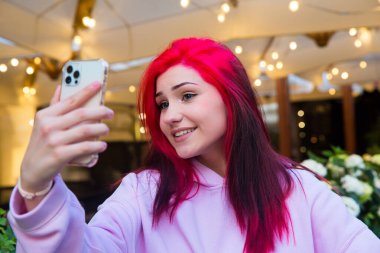 Güzel kızıl saçlı kız şehirde akıllı telefondan selfie çekiyor..