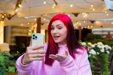 Güzel kızıl saçlı, etkili blog yazarı kafede konuşan kız sosyal ağlardaki aboneleriyle video görüşmesi yapıyor..