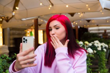 Güzel kızıl saçlı, etkili blog yazarı kafede konuşan kız sosyal ağlardaki aboneleriyle video görüşmesi yapıyor..