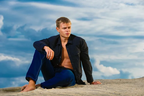 Stilig ung sitter på sanden på stranden. ser th — Stockfoto