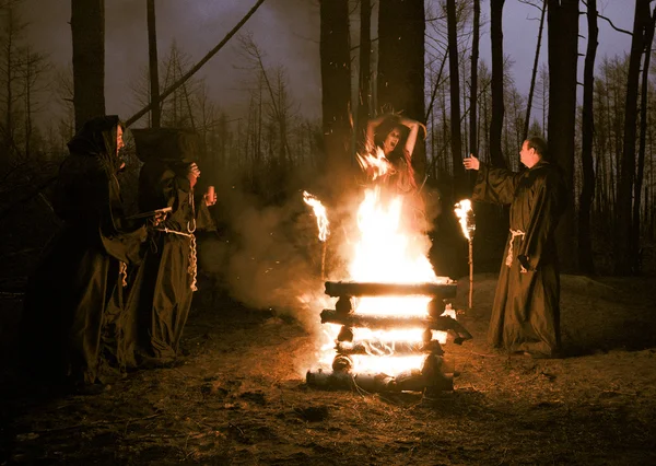 Dia das Bruxas. Homens vestidos de preto, queimam a bruxa na fogueira. — Fotografia de Stock