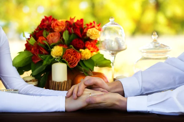 Mãos de homens e mulheres com anéis de casamento em uma mesa decorada — Fotografia de Stock