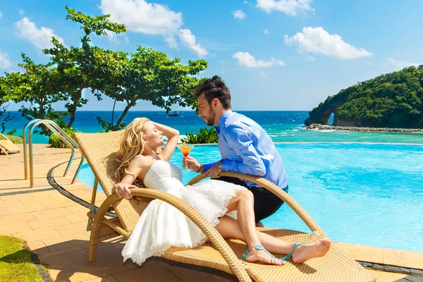 Happy bride and groom enjoy a cocktail poolside infinity. Tropic — Stock Photo, Image