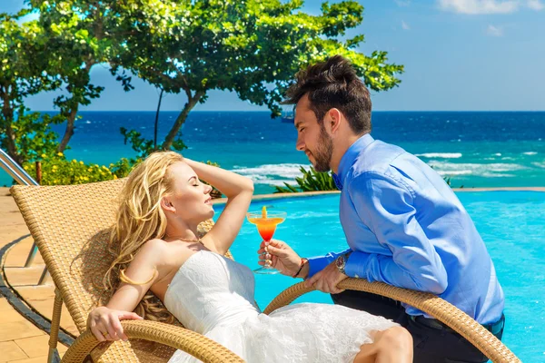 Happy bride and groom enjoy a cocktail poolside infinity. Tropic — Stock Photo, Image