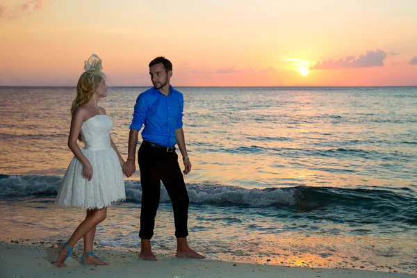 Bride and groom on a tropical beach with the sunset in the backg — Stock Photo, Image