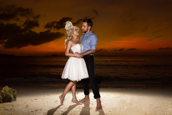 Bride and groom on a tropical beach with the sunset in the backg — Stock Photo, Image