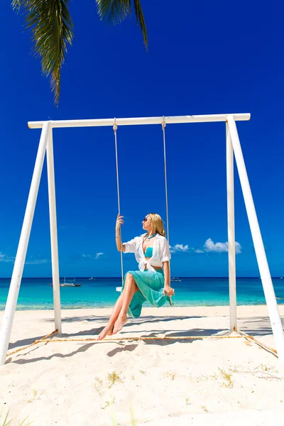 Giovane bella ragazza seduta su un'altalena sotto una palma. Blu — Foto Stock