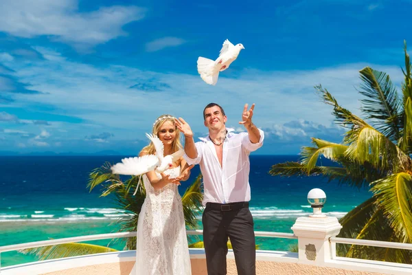 Šťastné nevěsty a ženicha s bílými holubicemi na tropické pláži u — Stock fotografie