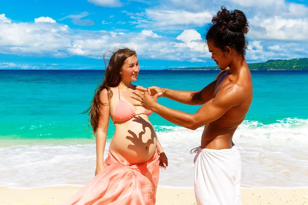 Glad och unga gravida par att ha kul på en tropisk strand. — Stockfoto