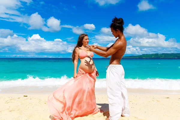 Glückliches und junges schwangeres Paar, das Spaß an einem tropischen Strand hat. — Stockfoto