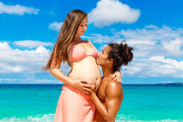 Glad och unga gravida par att ha kul på en tropisk strand. — Stockfoto