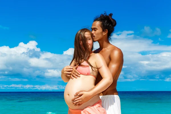 Glückliches und junges schwangeres Paar, das Spaß an einem tropischen Strand hat. — Stockfoto