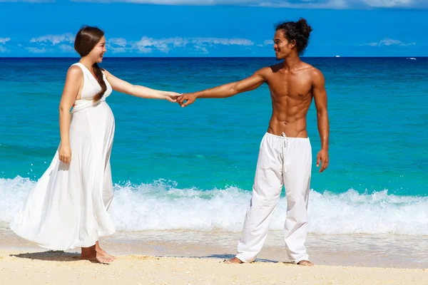 Glückliches und junges schwangeres Paar, das Spaß an einem tropischen Strand hat. — Stockfoto