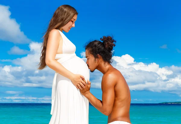 Glad och unga gravida par att ha kul på en tropisk strand. — Stockfoto