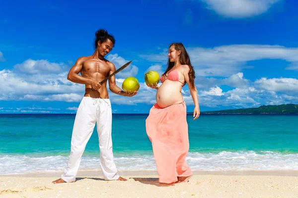 Happy and young pregnant couple with coconuts having fun on a tr — Stock Photo, Image