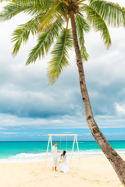 Szczęśliwy pana młodego i panny młodej na tropikalnej plaży pod palmą — Zdjęcie stockowe