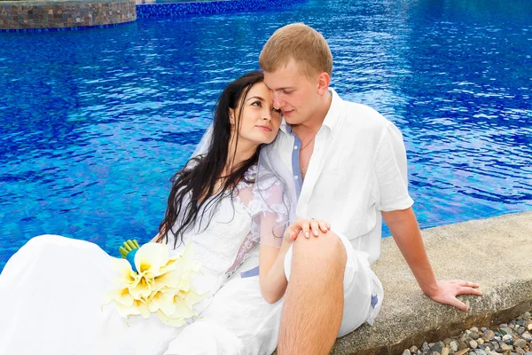 Boldog vőlegény és menyasszony ült a medence partján. Esküvő és nászút — Stock Fotó