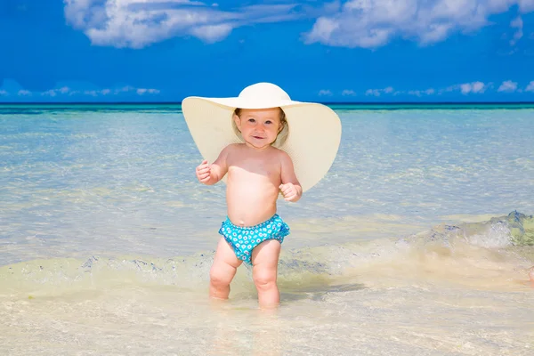 Ein kleines Kind in einem großen weißen Strohhut hat Spaß auf einem tropischen — Stockfoto