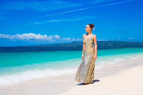 Mooi meisje in een gouden jurk op het strand van een tropische is — Stockfoto